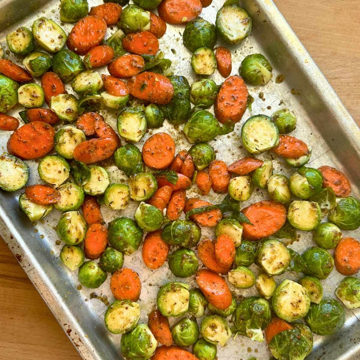 Brussels sprouts and carrots coated with maple Dijon glaze on a sheet pan.