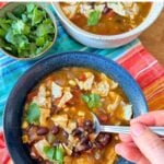 Vegan black bean tortilla soup in a blue bowl with a spoon over a bright red, orange, and blue napkin.