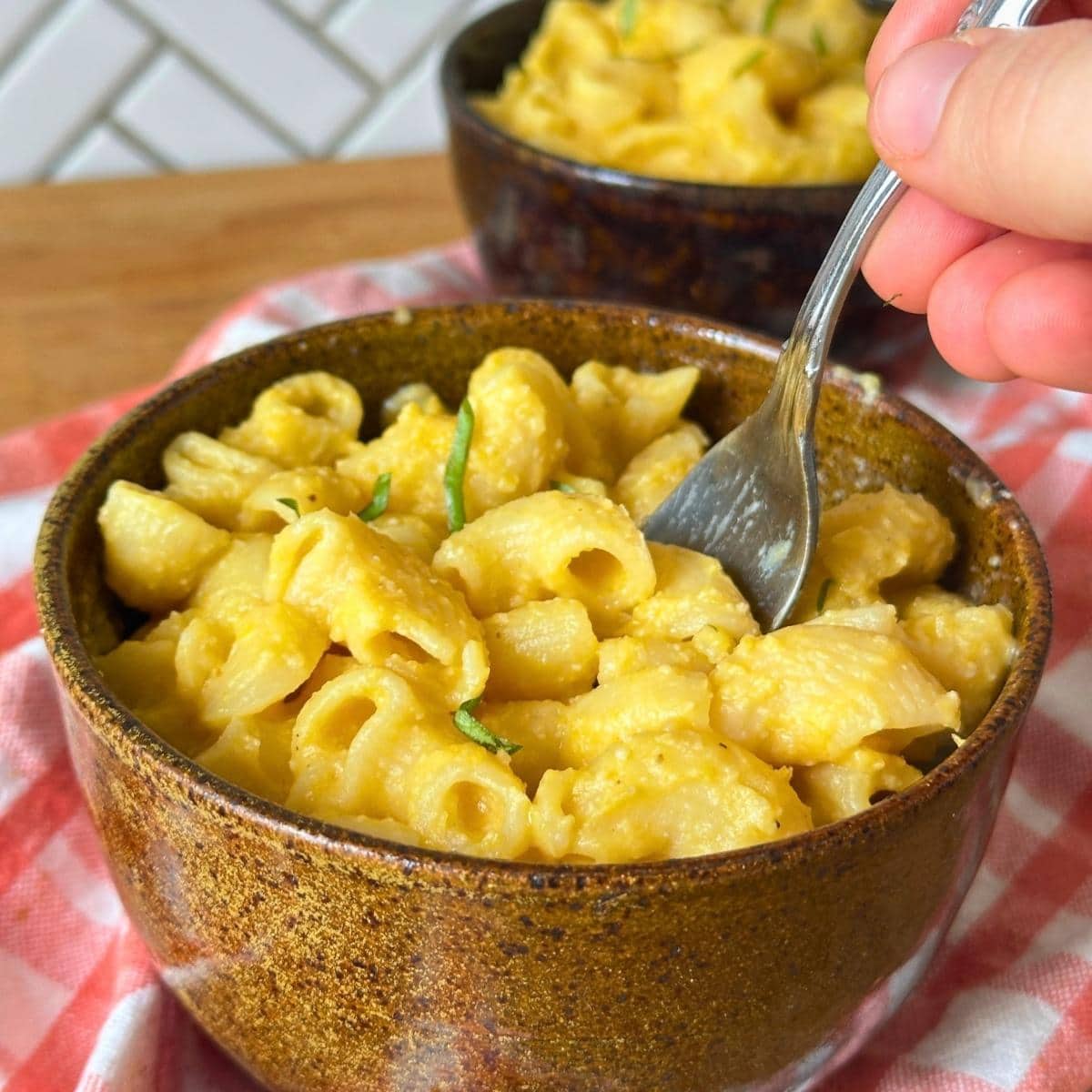 Bowl of creamy vegan butternut squash mac and cheese with sliced basil leaf on top.