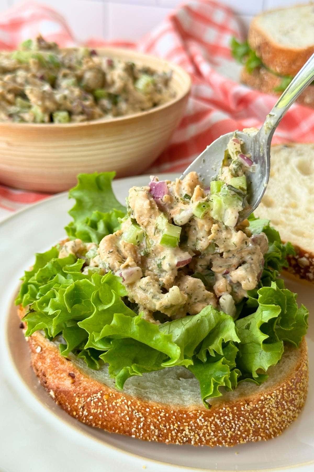 Vegan chicken salad with soy curls being spooned onto a piece of bread with lettuce.