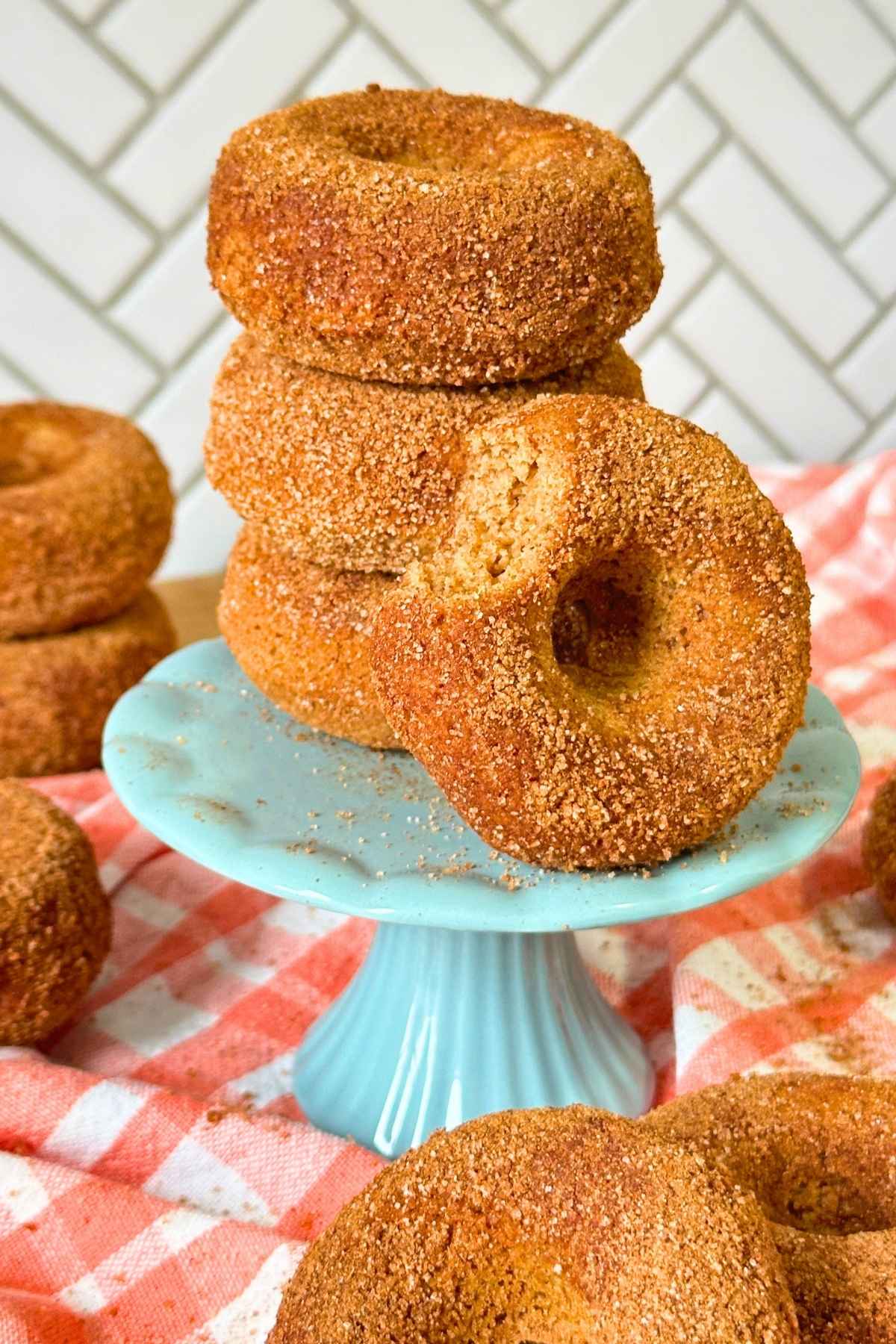 Stack of three vegan gluten-free apple cider donuts on a blue pedestal with another donut with a bite taken out of it resting on the side.