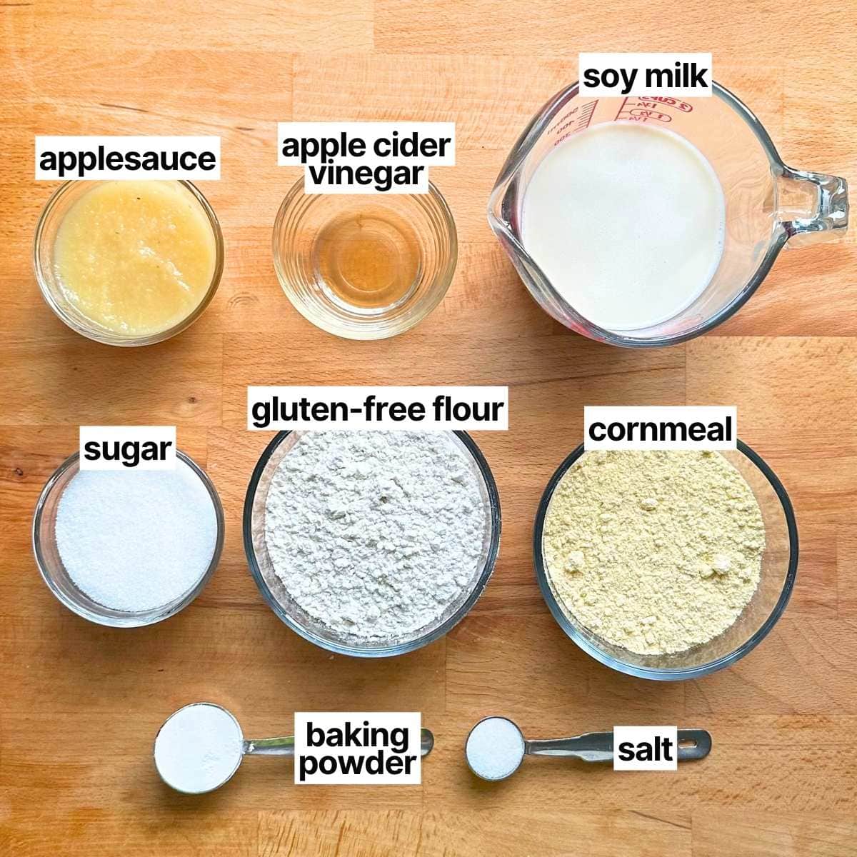 Ingredients to make vegan gluten-free cornbread with corresponding labels: applesauce, apple cider vinegar, soy milk, sugar, gluten-free flour, cornmeal, baking powder, and salt.
