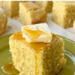 Cube of vegan gluten-free cornbread with butter and maple syrup dripping onto a green plate.