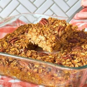 Square of vegan pumpkin baked oatmeal being lifted out of a pan of more baked oatmeal squares.
