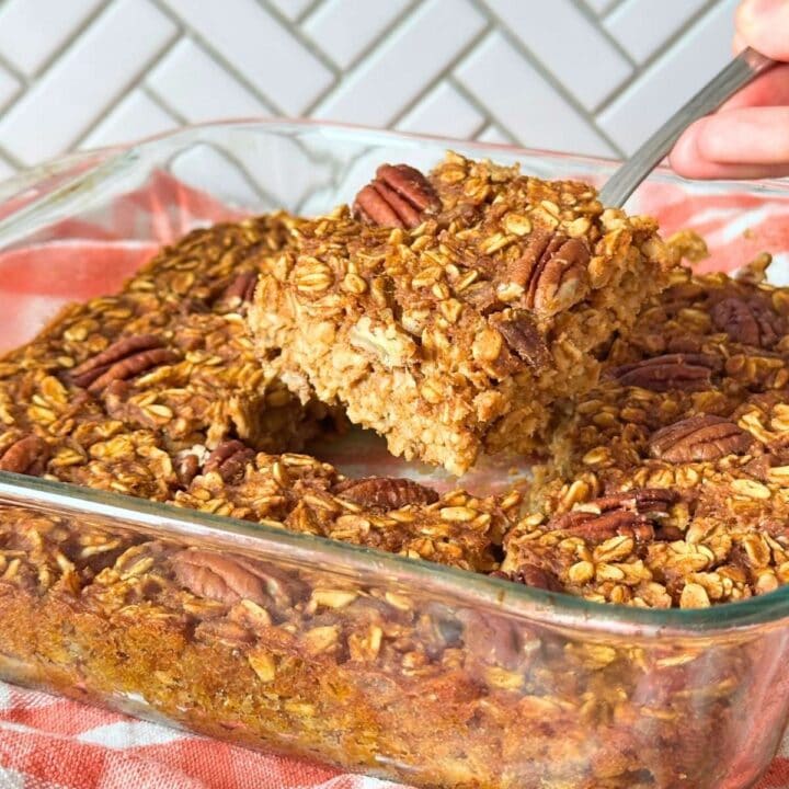 Square of vegan pumpkin baked oatmeal being lifted out of a pan of more baked oatmeal squares.