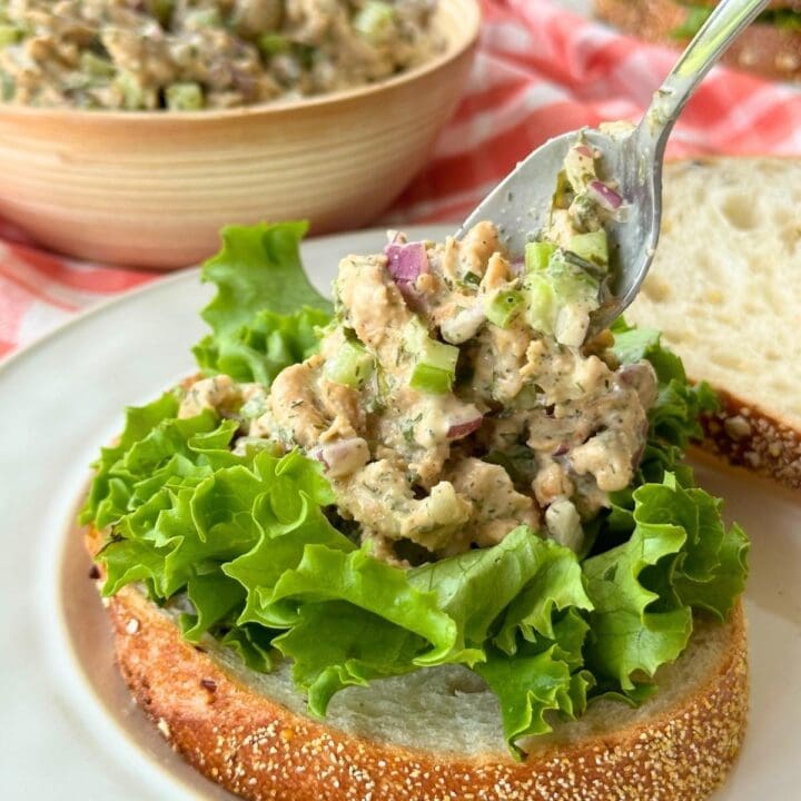 Vegan chicken salad with soy curls being spooned onto a piece of bread with lettuce.