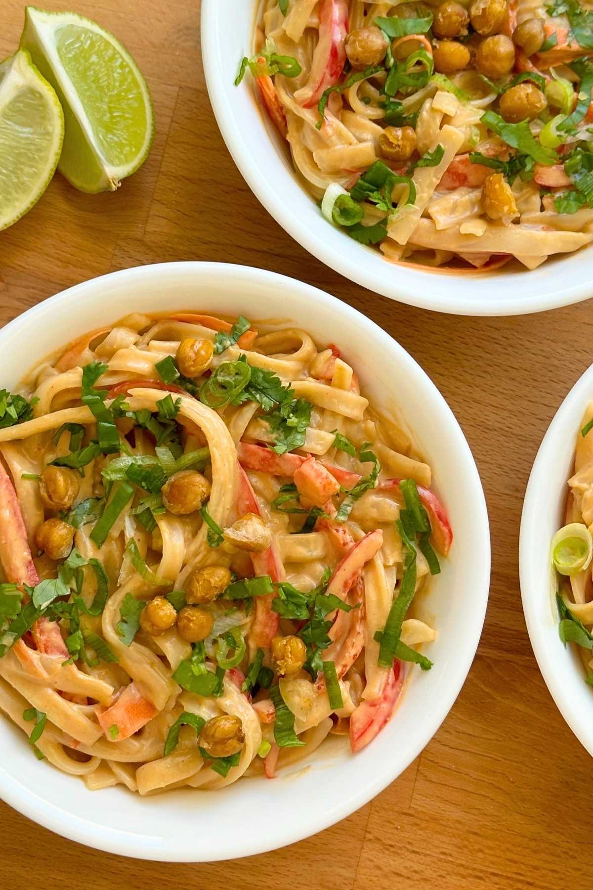 Vegan Thai peanut noodles in 3 bowls with red bell peppers, chickpeas, green onions, and cilantro on top.