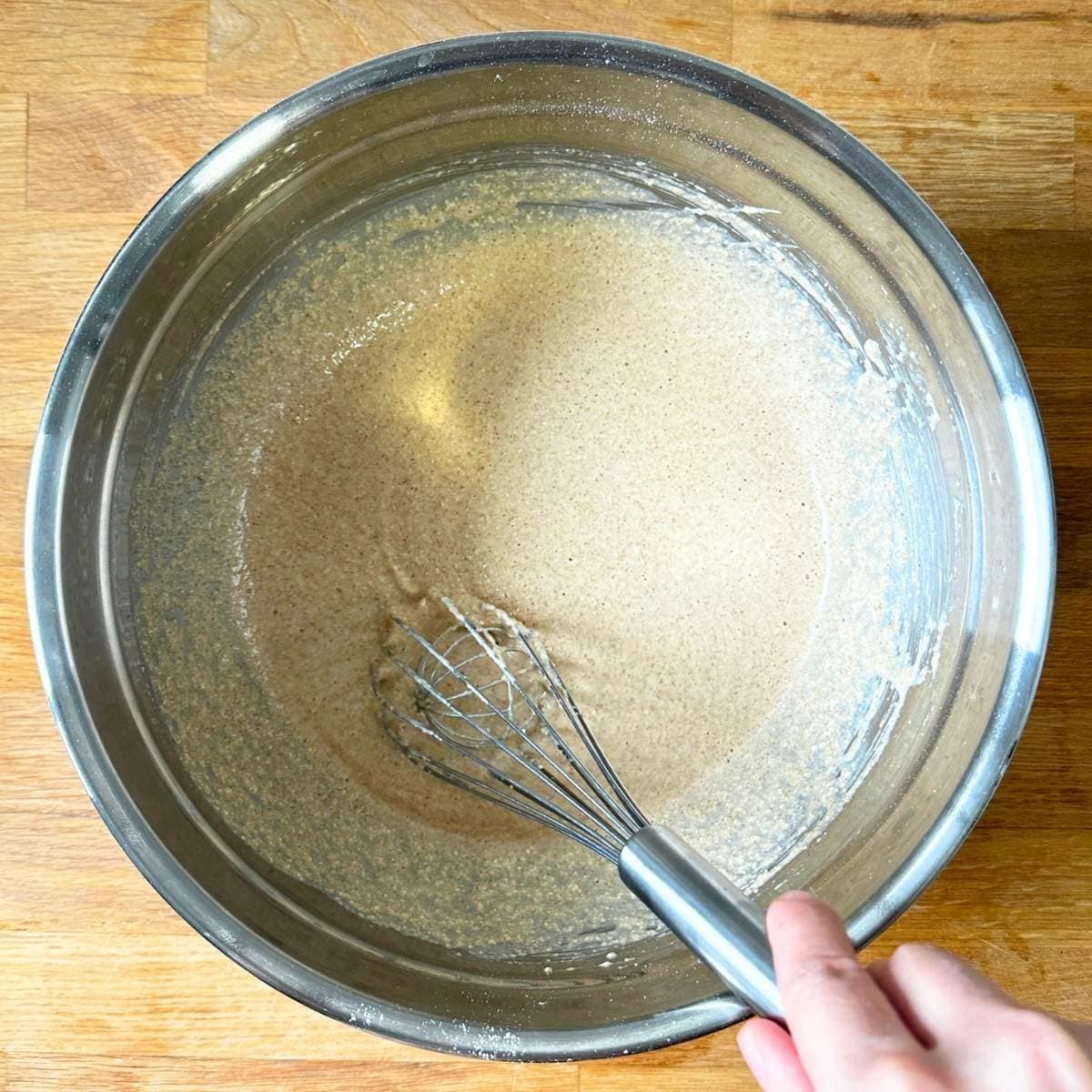 Whisking gluten-free apple cider donut batter in a metal bowl.