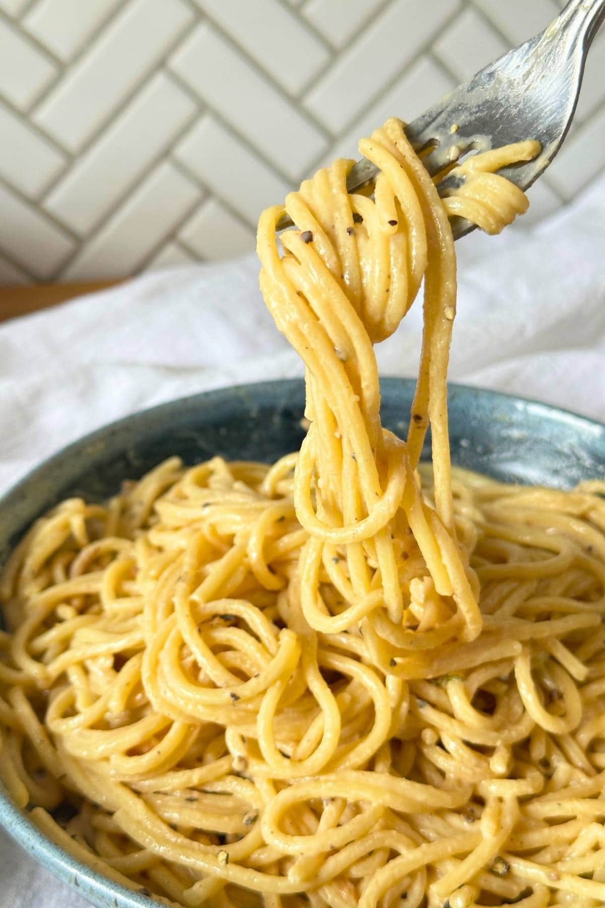 Fork with vegan cacio e pepe twisted around it lifting it up from a bowl of pasta.