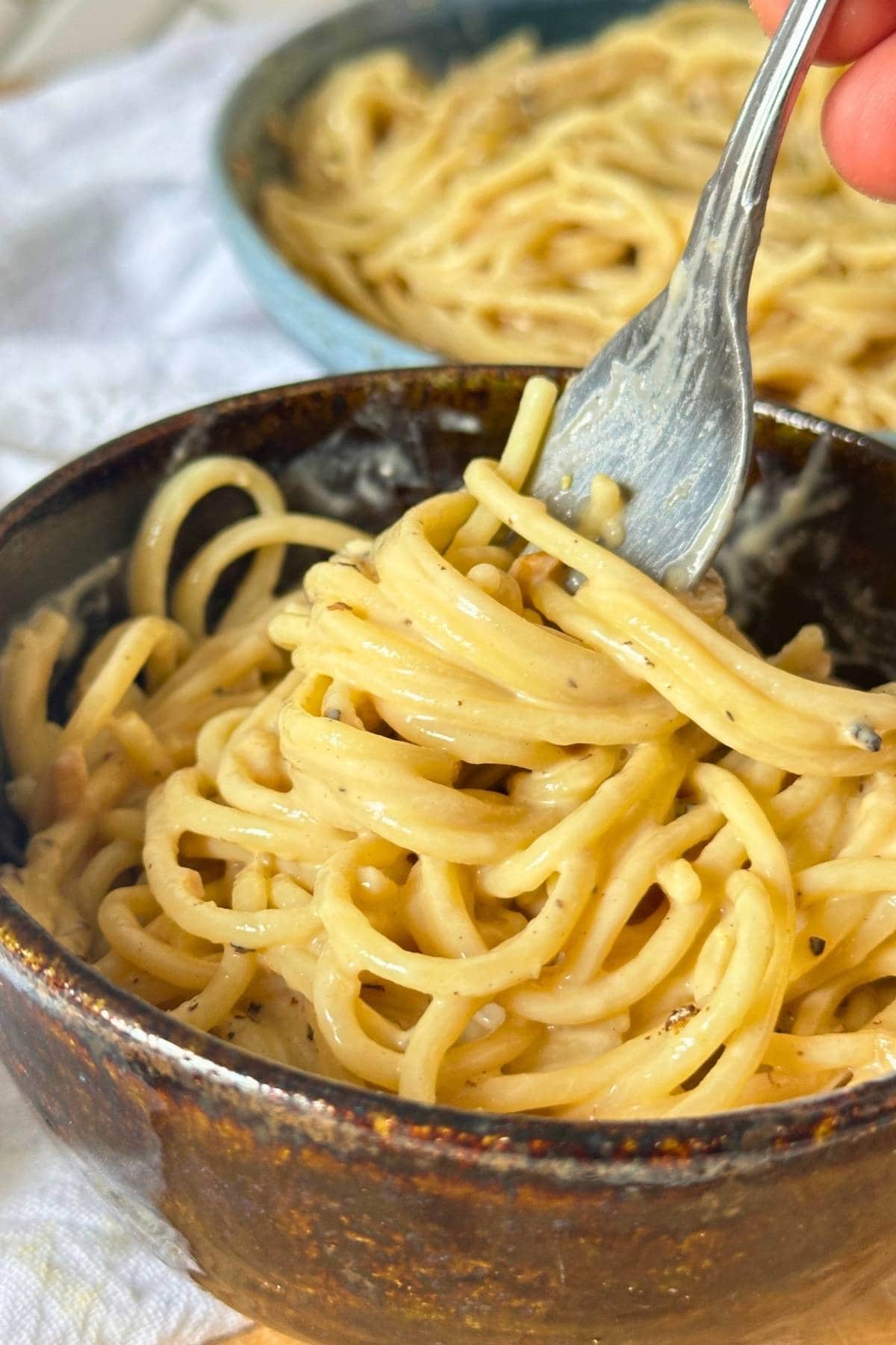 Bowl with creamy vegan cacio e pepe made with cashews with a fork.