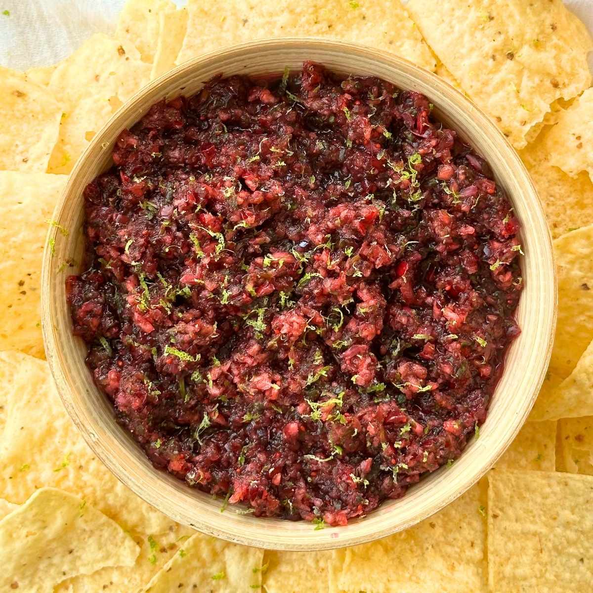 Cranberry salsa in a bowl with lime zest on top and chips around the bowl.