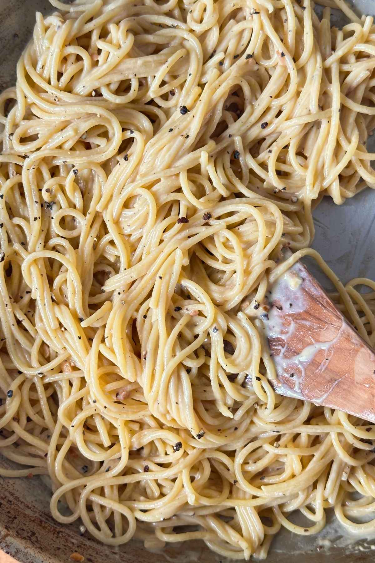 Pasta combined with cashew sauce, garlic, and pepper in a pan on the stovetop.