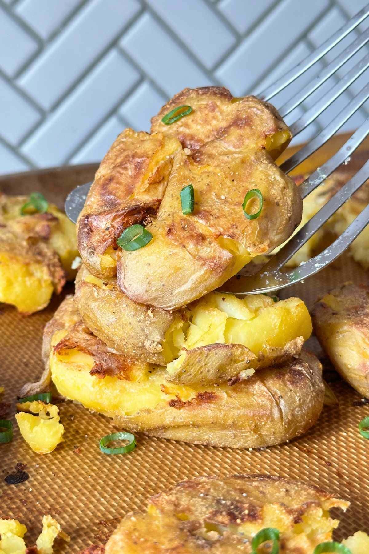 Stack of three garlic smashed potatoes with a metal spatula picking up the top one.