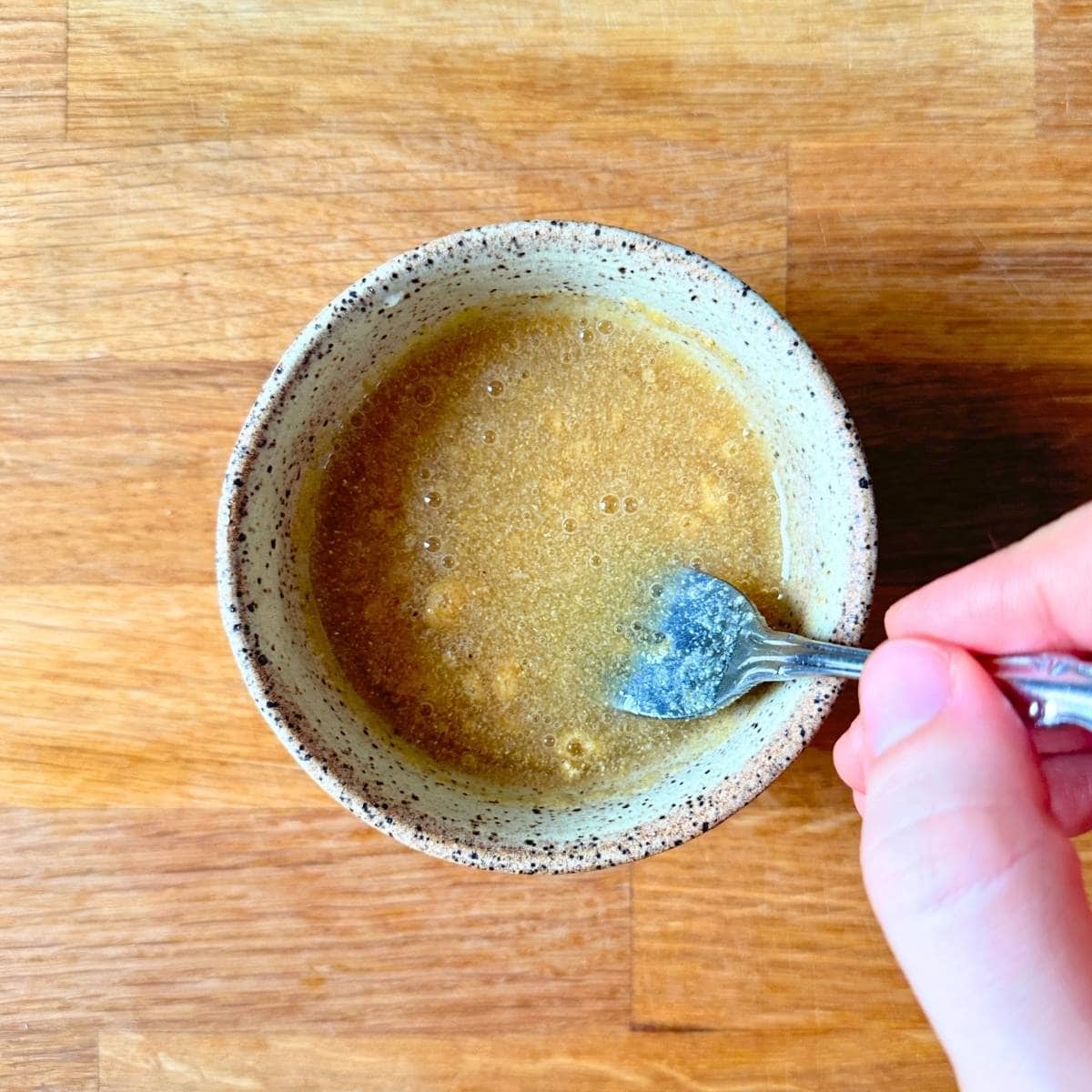 Mixing aquafaba and garlic powder in a small bowl with a fork.
