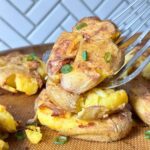 Stack of three garlic smashed potatoes with a metal spatula picking up the top one.