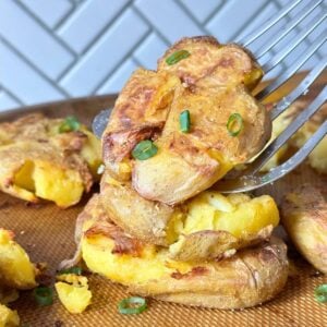 Stack of three garlic smashed potatoes with a metal spatula picking up the top one.