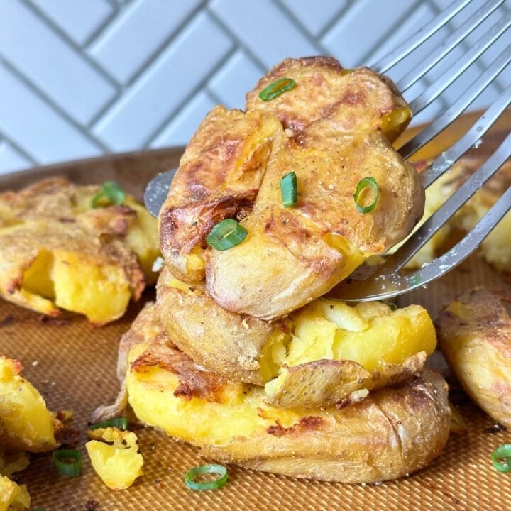 Stack of three garlic smashed potatoes with a metal spatula picking up the top one.
