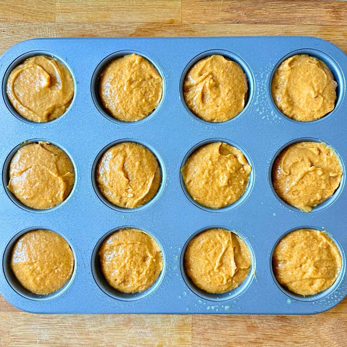 Pumpkin muffin batter scooped into a muffin tin.
