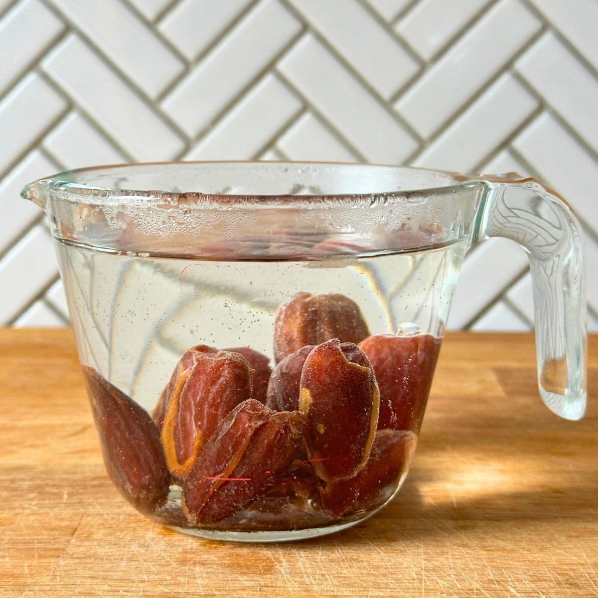Soaking Medjool dates in a measuring cup filled with hot water.